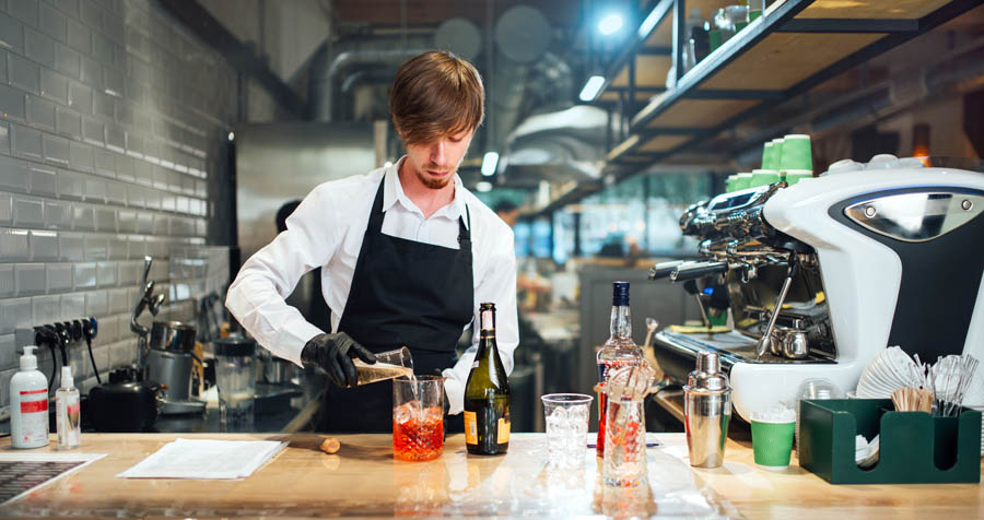 Barman pours the ingredients of the cocktail into a glass for mixing. Professional cocktail preparation process.