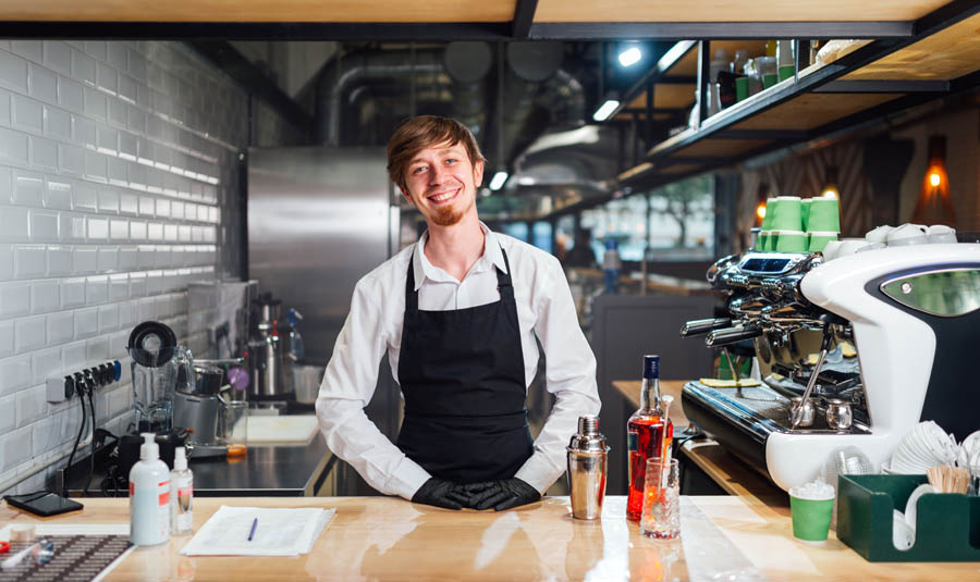 Cheerful bartender barista behind the counter. Work in the kitchen of public catering